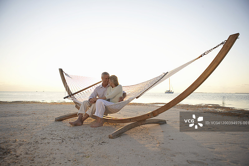 一对中年夫妇坐在海滩吊床上，头靠在一起图片素材
