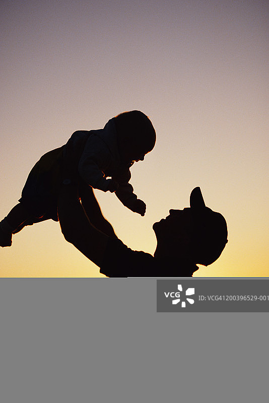 父亲在海滩边抱着男婴（6-9个月），日落图片素材