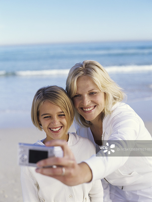 女人和女儿(10-12岁)在海滩上自拍，微笑图片素材