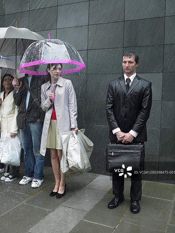 撑着伞看着淋湿的商人的年轻女人图片素材