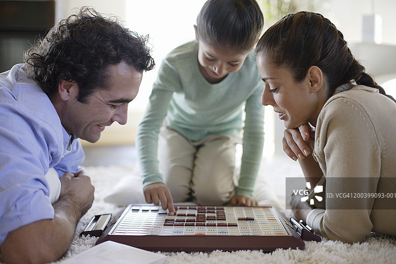 家人在地板上玩简单的棋盘游戏，侧视图（焦点在情侣身上）图片素材