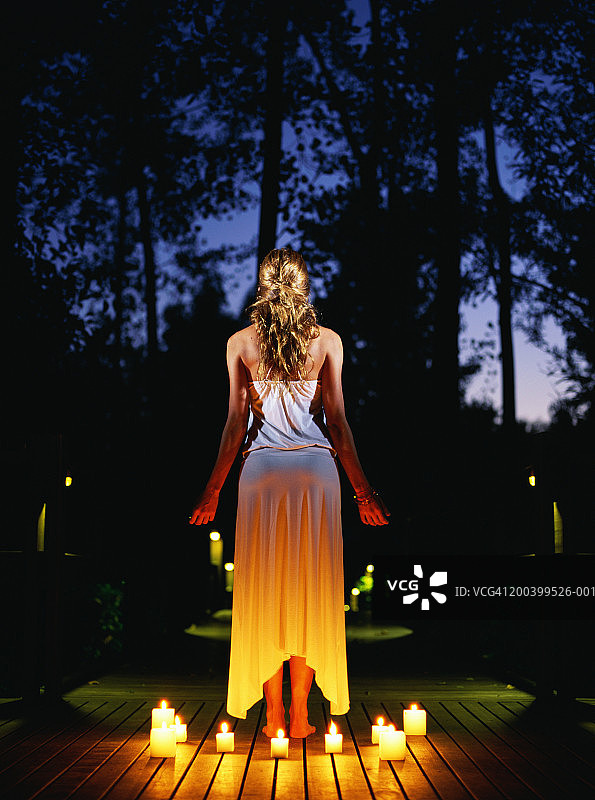 黄昏时分站在被蜡烛包围的露台上的女人（后视图）图片素材