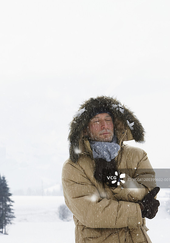 雪地乡村景观中闭着眼睛的连帽夹克男人图片素材