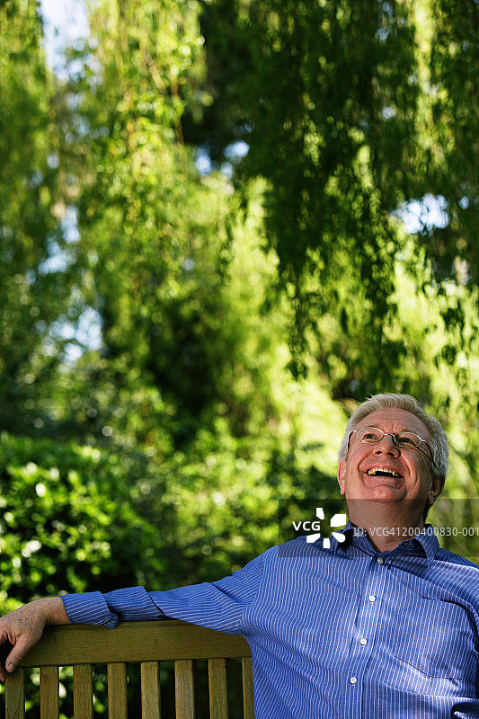 老年男人坐在花园长椅上微笑图片素材