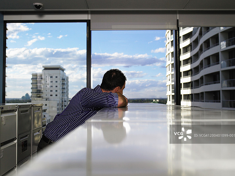 年轻男人靠在文件柜上，看向窗外图片素材