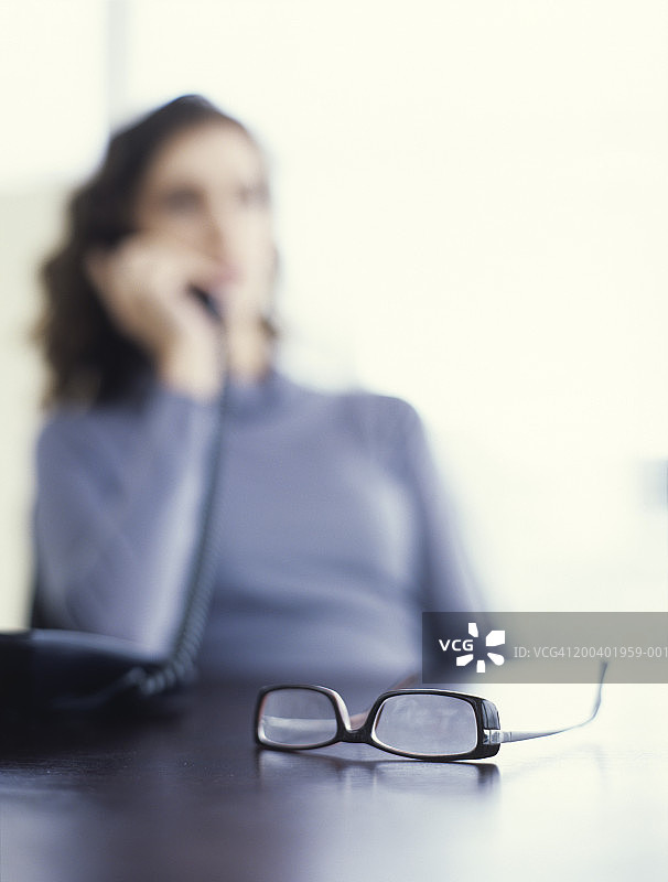 戴眼镜的女人坐在桌旁打电话特写图片素材