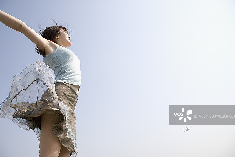 年轻女子在户外跳跃，张开双臂图片素材