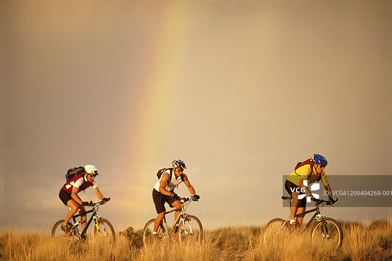 三个男人在田野里骑山地自行车，背景是彩虹图片素材