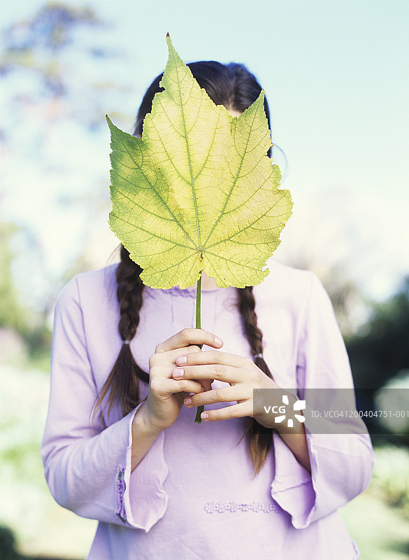 拿着树叶挡住脸的女孩（9-11岁）图片素材