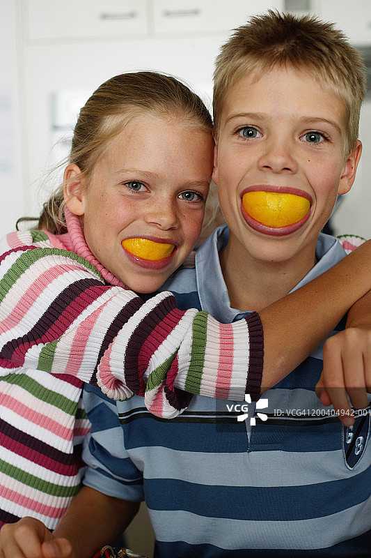 嘴里含着橙子的双胞胎兄妹（10-12岁），特写图片素材
