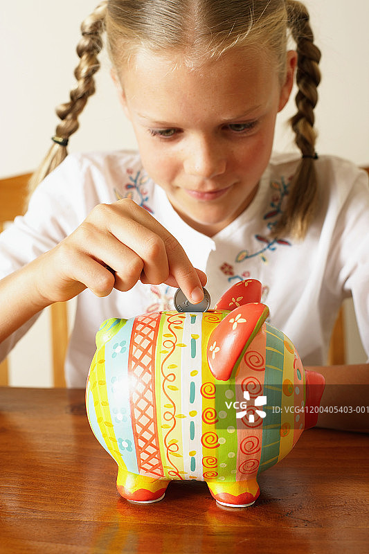 女孩（10-12岁）将硬币投入储蓄罐，特写图片素材