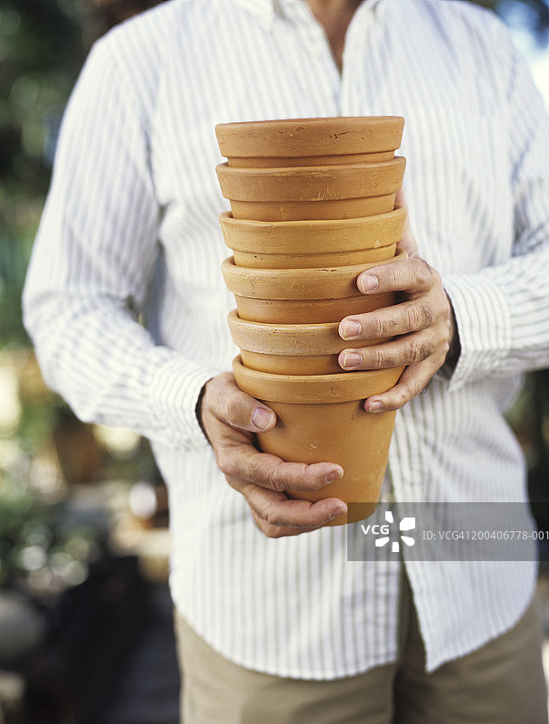 手持一叠赤陶盆的年长男人特写，中部视角图片素材