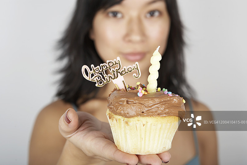 女人手持带蜡烛的纸杯蛋糕和生日快乐标牌人像图片素材