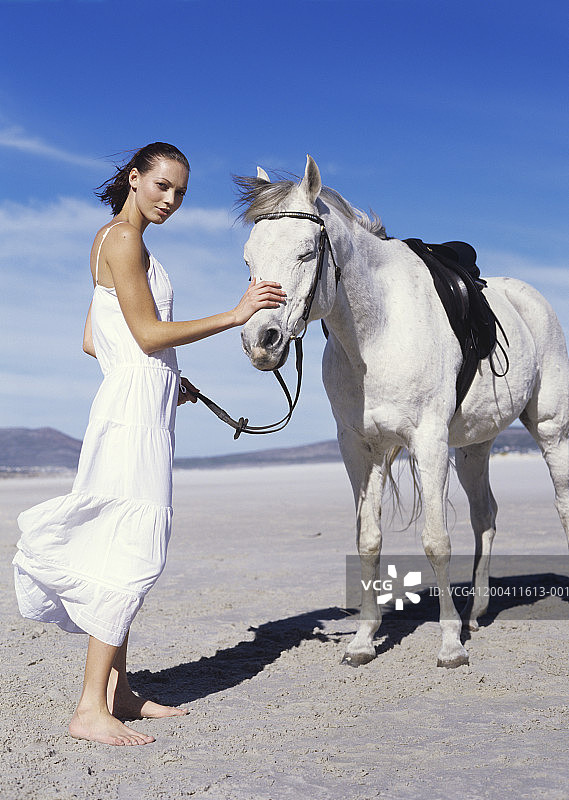 年轻女子在海滩上抚摸马匹图片素材