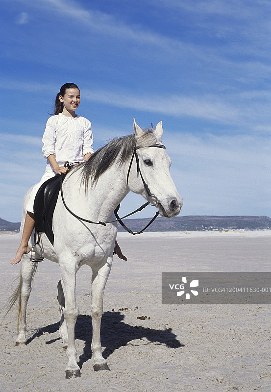 女孩（9-10岁）坐在海滩的马背上微笑图片素材