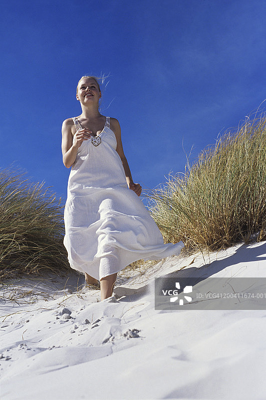 年轻女人在沙丘中奔跑，微笑，低角度拍摄图片素材