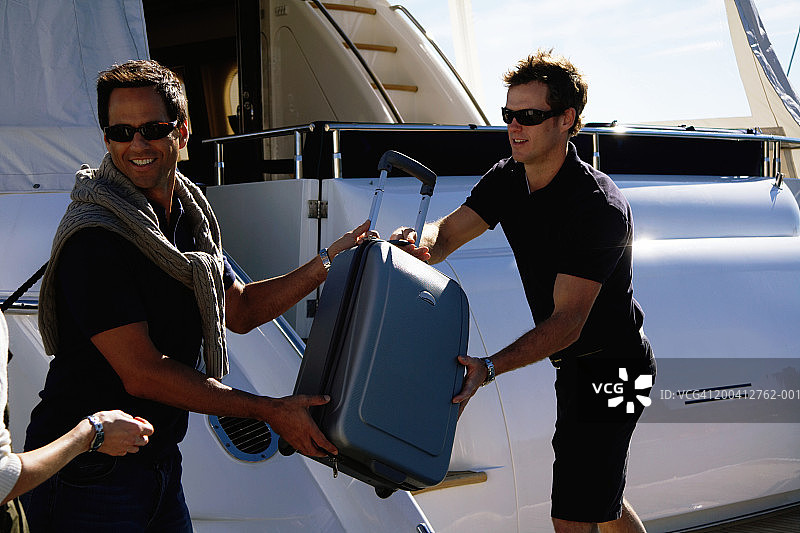 年轻男人微笑地将行李装载到游艇上图片素材