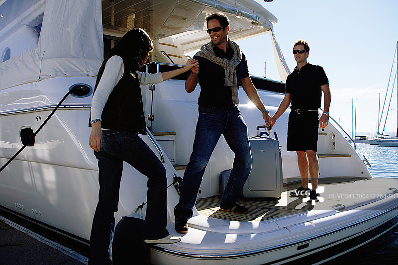 在码头，中年男人帮助中年妇女登上游艇，面带微笑图片素材