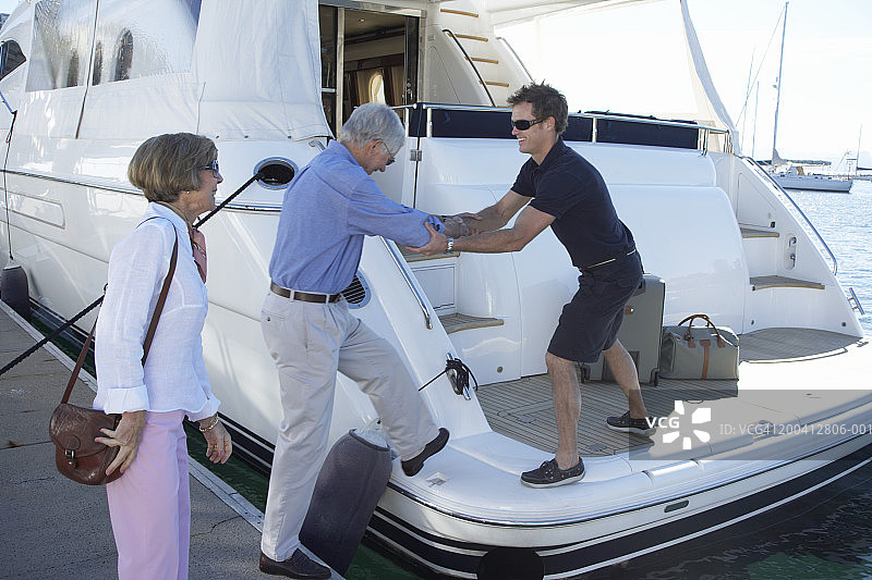 游艇上，男船员帮助老年男人，前景是女人图片素材
