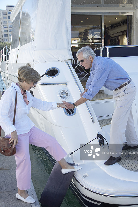 老年男人在海港帮助老年妇女登上游艇，面带微笑图片素材