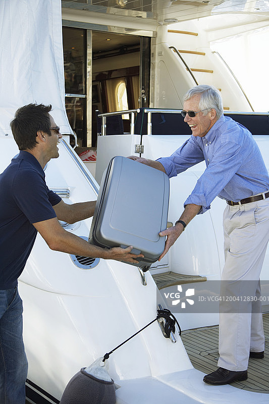 年长的男人帮助中年男人将行李装上游艇，面带微笑图片素材