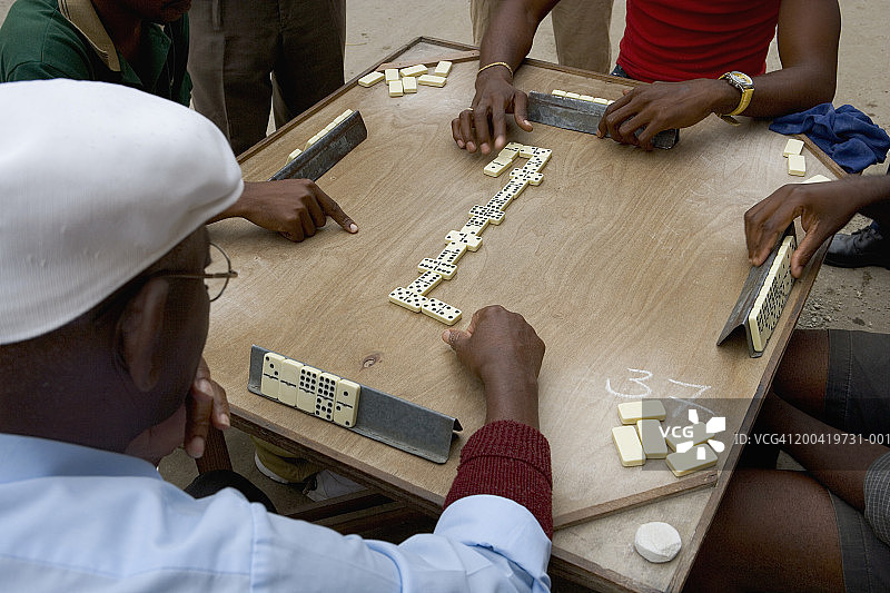 四名男子在街边的桌旁玩多米诺骨牌，从男人的肩膀上方看图片素材