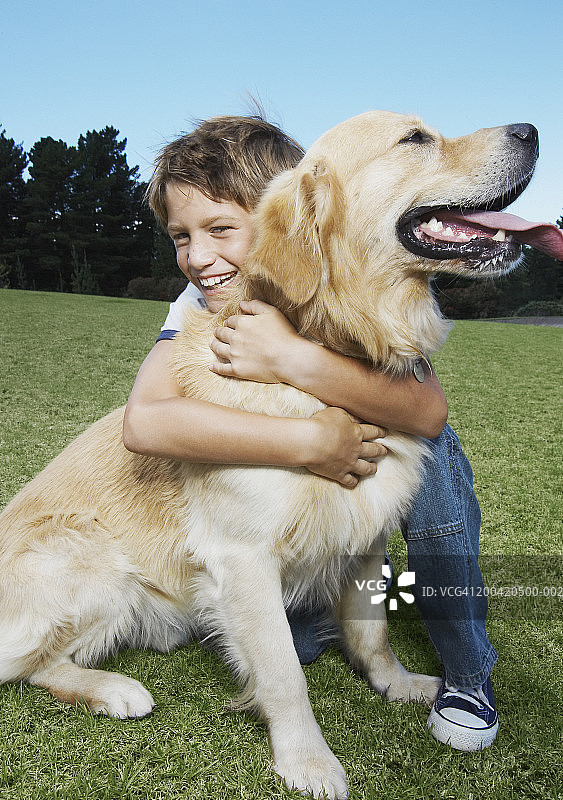 拥抱金毛寻回犬的微笑男孩（8-10岁）肖像图片素材
