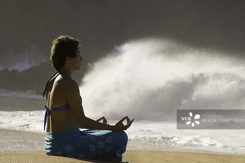 年轻女人在海滩上冥想，靠近海浪图片素材