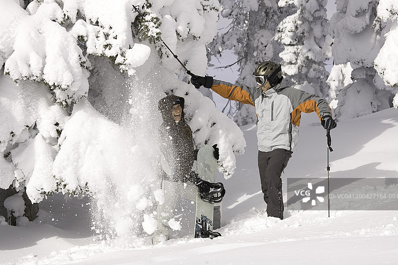 男人用滑雪杖敲打树枝，将雪落在下面的女人身上图片素材