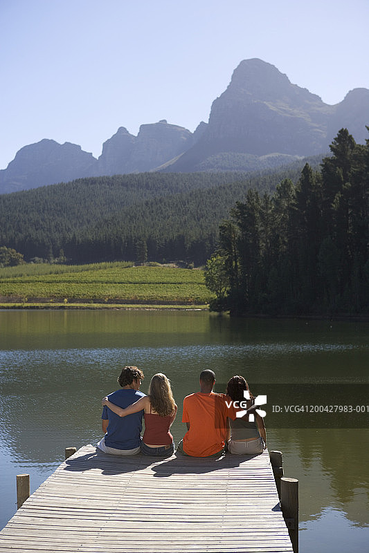 年轻情侣坐在码头上，后视图图片素材