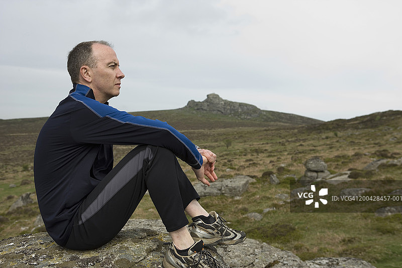 英国德文郡达特穆尔海托谷，男子坐在岩石上侧视图片素材
