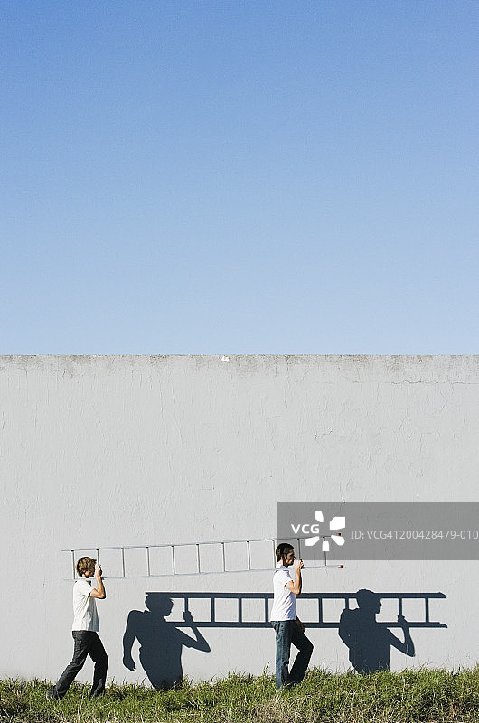 两个男人肩扛梯子，靠墙的侧影图片素材