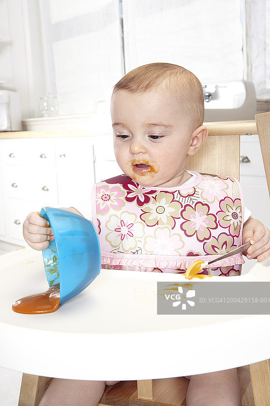 坐在高脚椅上，将碗倾倒在托盘上的女婴（5-7个月）图片素材