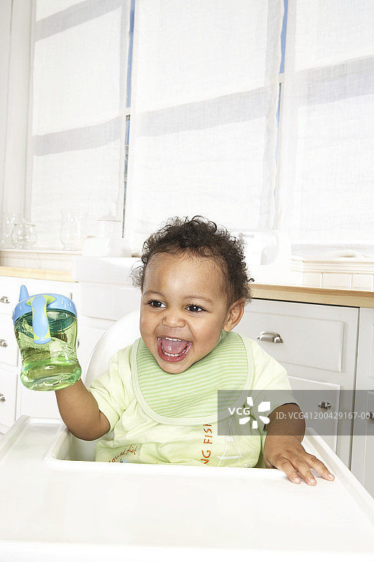 18-24个月男婴坐在高脚椅上拿着杯子微笑图片素材