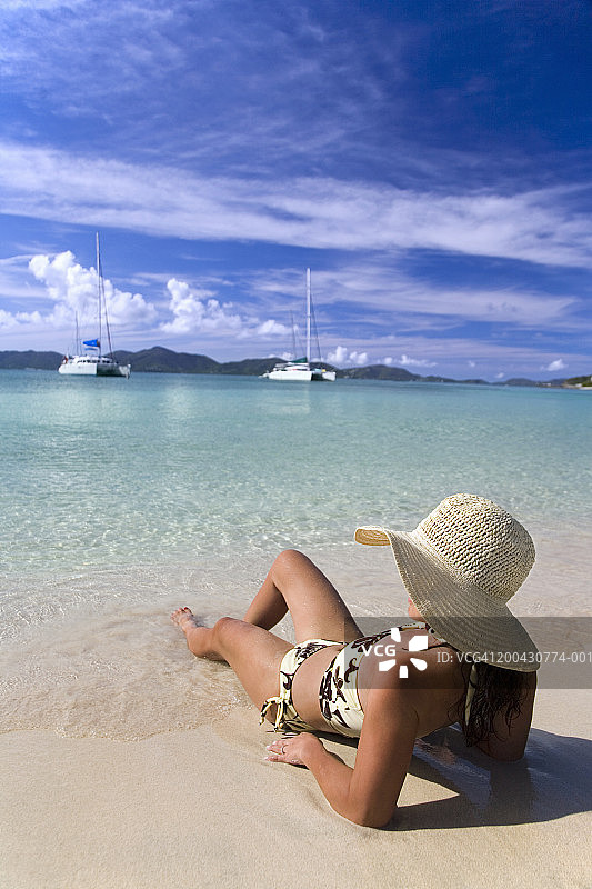 戴着帽子躺在海滩上的女人，后视图图片素材