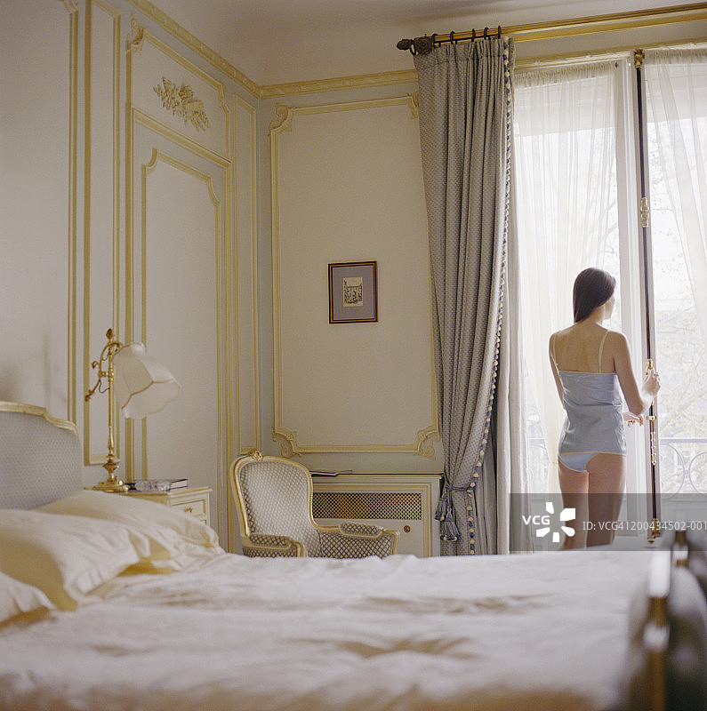 年轻女子在卧室窗口向外看，后视图图片素材