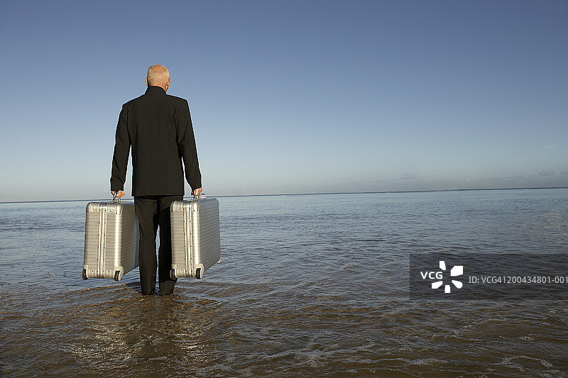 年长的男人在海滩上提着行李箱，后视图图片素材