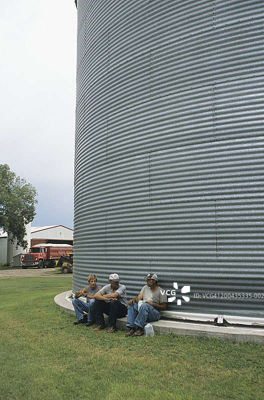 坐在粮仓旁边的三个男性农民图片素材