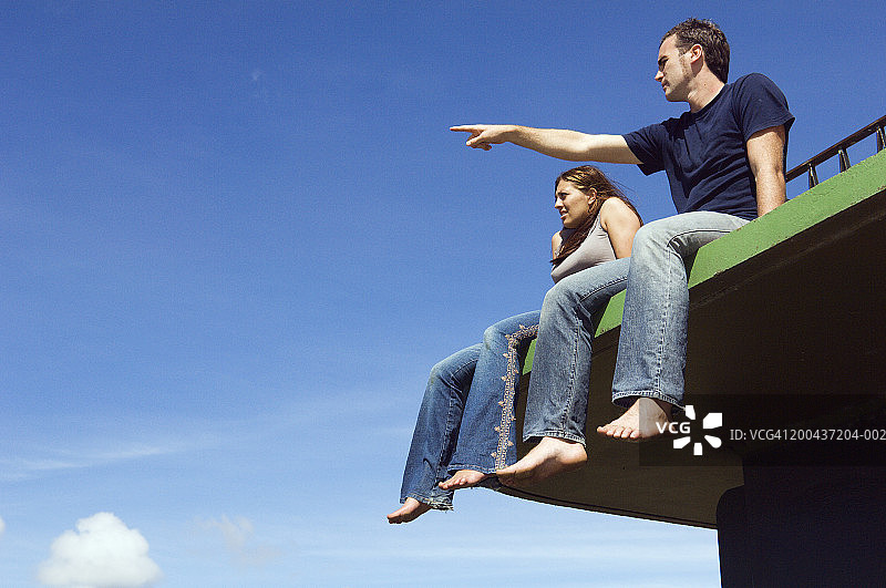 情侣坐在户外平台上，男人手指前方图片素材