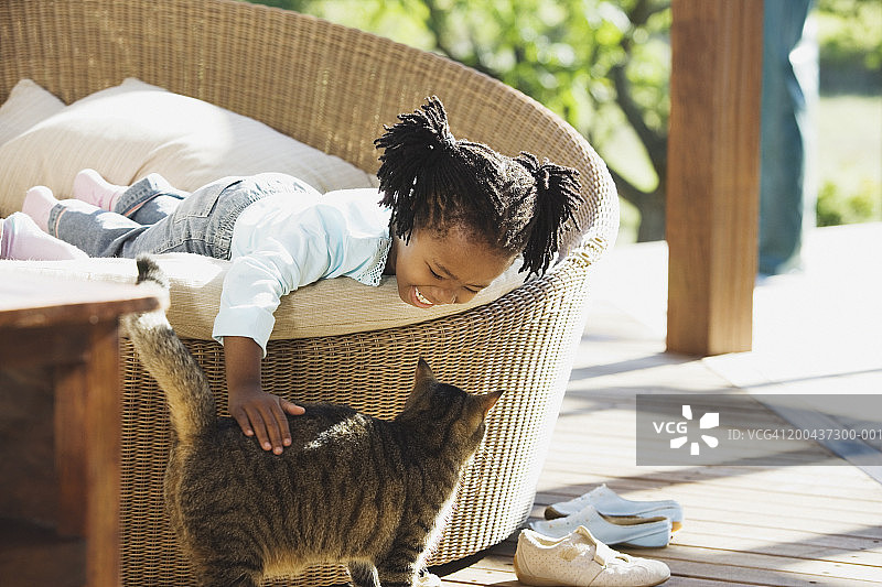 女孩躺在阳台的座位上抚摸着猫，面带微笑图片素材