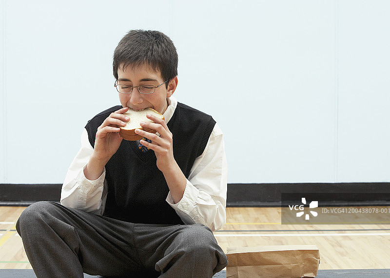 男孩（11-13岁）在学校体育馆吃三明治，闭着眼睛图片素材