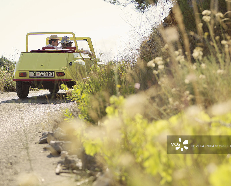 情侣在乡间道路上驾驶敞篷车（后视图，地面视角）图片素材