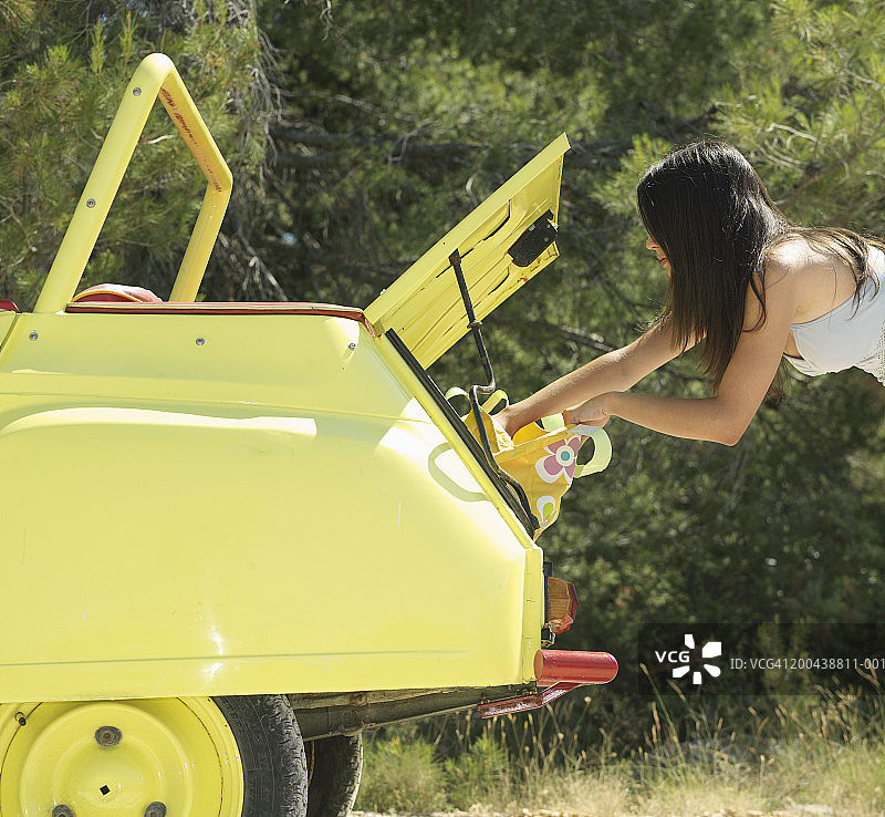 在打开的后备箱旁弯腰查看包的年轻女人（侧面视角）图片素材