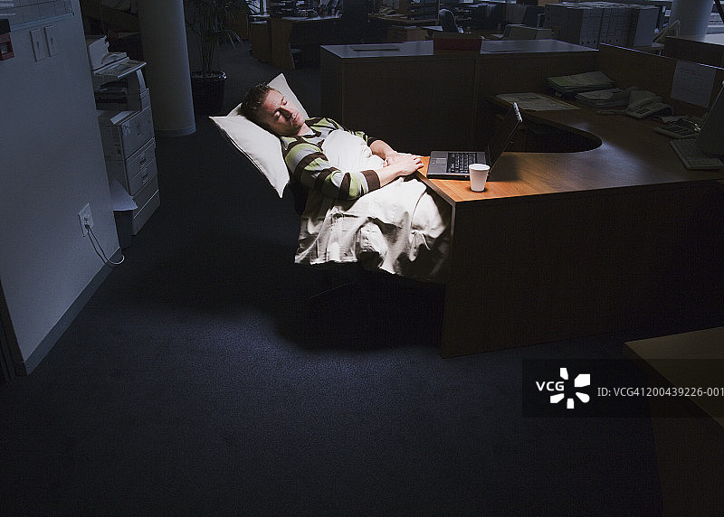 男子在办公室的桌子上睡觉，使用枕头和被子图片素材