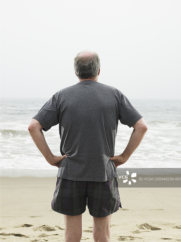 中年男人站在海滩上，后视图图片素材