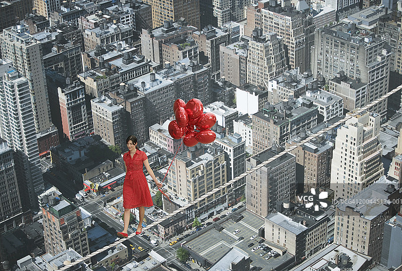 手捧一束气球，走在城市景观上钢索的年轻女人图片素材