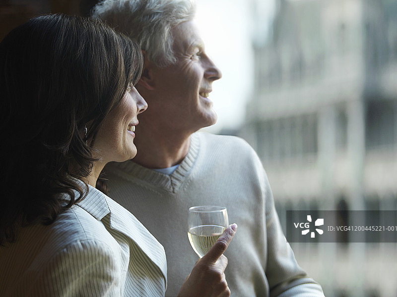 窗边手持葡萄酒杯微笑的中年夫妇图片素材