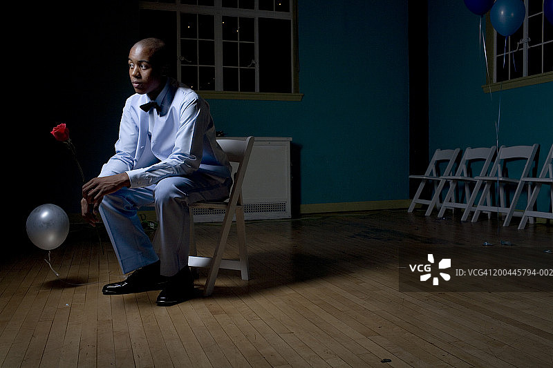 身穿燕尾服手持玫瑰坐在折叠椅上的青少年男孩图片素材