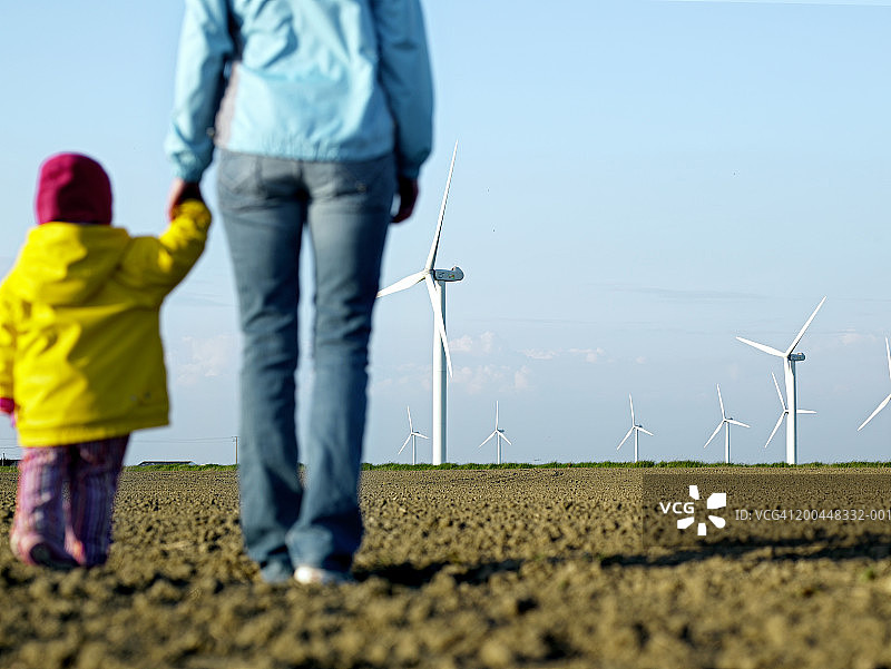 小女孩牵着妈妈的手，看着风力发电场，后视图图片素材