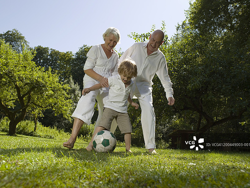 祖父母在花园里和微笑的孙子(3-5岁)踢足球图片素材